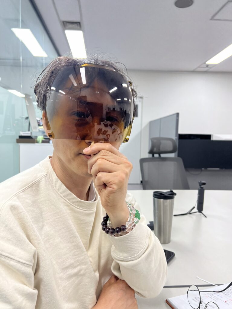 폴리카보네이트 고글 렌즈의 강도를 확인하기 위해 휘어진 렌즈를 손에 들고 있는 남성 – 실험 후에도 깨지지 않은 렌즈의 내구성을 보여주는 장면